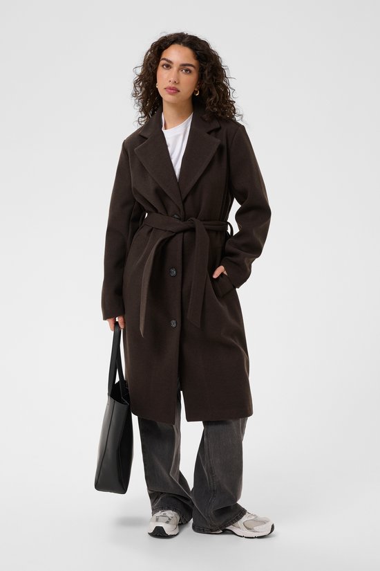 Model draagt een donkerbruine jas met ceintuur, grijze broek, sneakers en zwarte handtas.