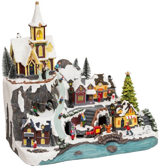 Verlicht kerstdorp met kerk, besneeuwde bergen, treintje, winkeltjes en schaatsers bij een rivier.