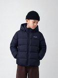 Jongen met donkerblauwe, gewatteerde jas met capuchon en Studio Outdoors logo, draagt zwarte muts.