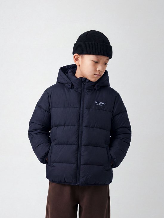 Jongen met donkerblauwe, gewatteerde jas met capuchon en Studio Outdoors logo, draagt zwarte muts.