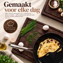 Snijplank van walnoothout met een koekenpan, omelet, eieren en verse kruiden.