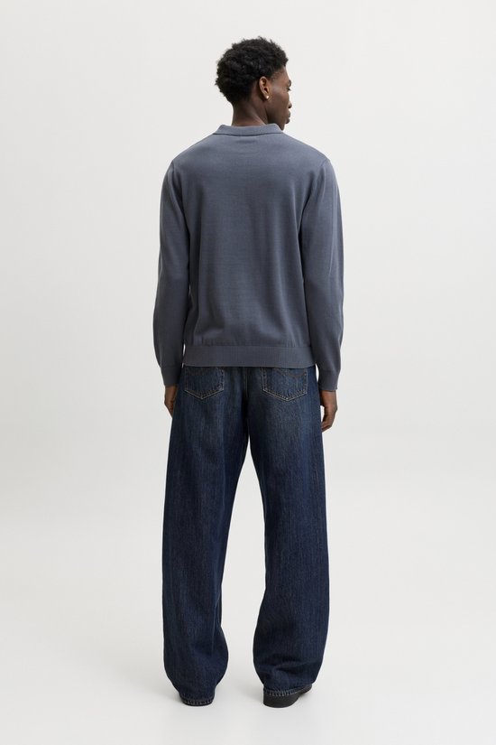 Achterkant van een man in een donkerblauwe gebreide polo en wijde jeans.