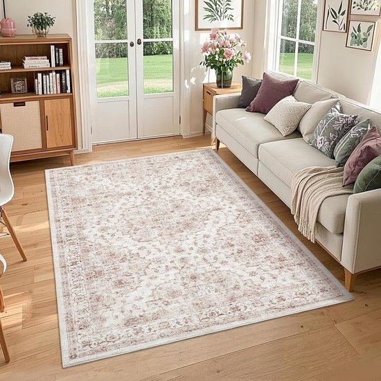 Een woonkamer met een roze en beige boho vloerkleed op een houten vloer, bij een crème bank en een houten kast.