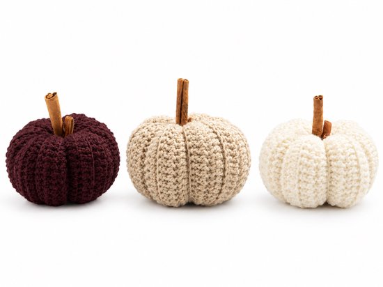 Drie gehaakte decoratieve pompoenen in bordeauxrood, beige en wit met kaneelstokjes als steeltjes.