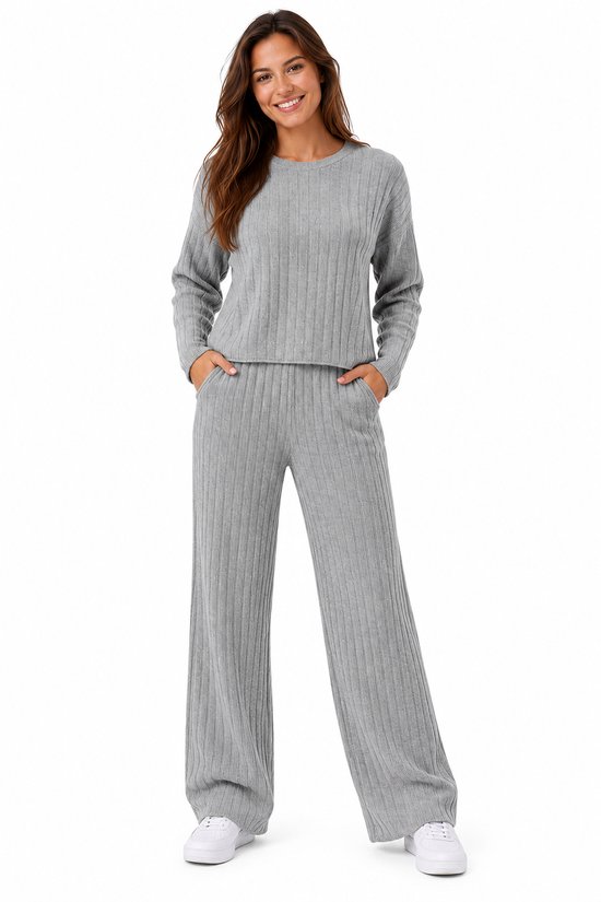 Model draagt een grijze, geribbelde lounge set bestaande uit een trui met lange mouwen en een broek met wijde pijpen.