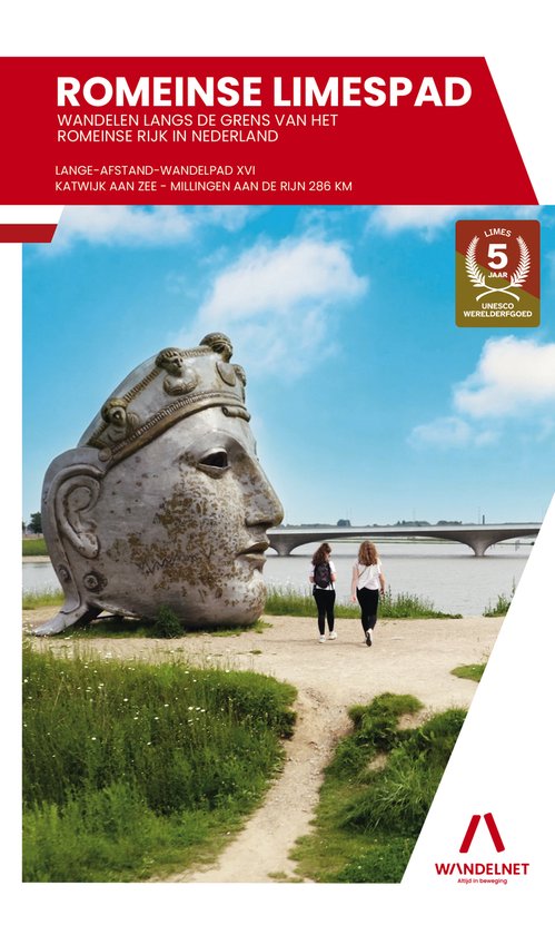 Twee vrouwen lopen op een pad langs een groot Romeins hoofdbeeld. Op de achtergrond een brug en blauwe lucht.