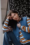Model in een donkerblauwe teddy bodywarmer over een gestreept shirt met oranje, witte en blauwe strepen.