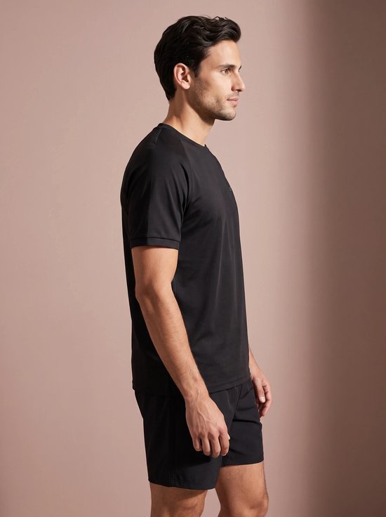 Man in profiel, draagt zwart sportshirt met logo op de borst en zwarte sportshort.