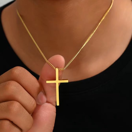 Gouden kruishanger met een glanzende afwerking aan een gouden ketting, gedragen door een persoon.