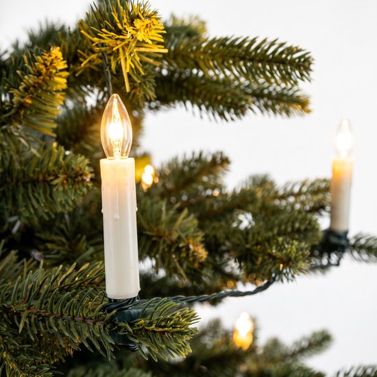Close-up van een brandend kaarslampje aan een tak van een kunstkerstboom.