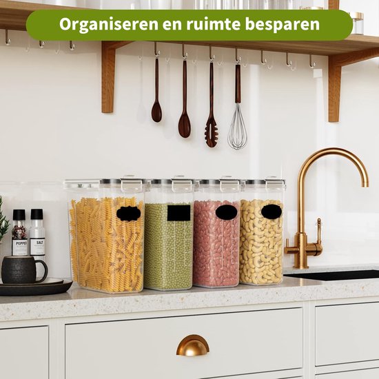 Vier doorzichtige voorraadcontainers gevuld met pasta, groene bonen, rode bonen en cashewnoten, opgesteld op een keuken aanrecht.