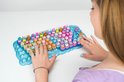 Vrouw speelt met een blauw Clickeez toetsenbord gevuld met felgekleurde figuurtjes.