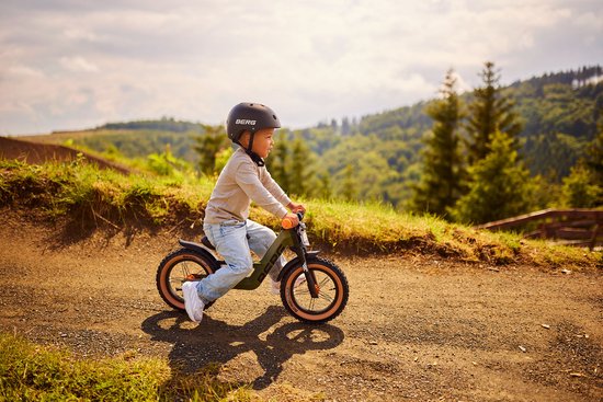 Jongen op een groene BERG Biky loopfiets met oranje handvaten, rijdend op een heuvelachtig off-road parcours.