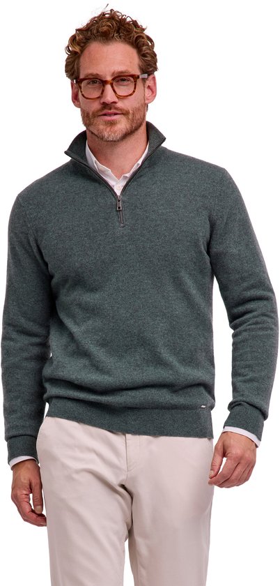 Model draagt een groene FALKE trui met rits over een wit overhemd en een beige broek.