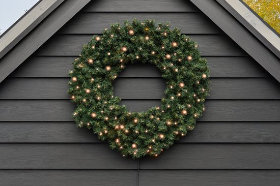 Kunstkerstkrans van 100 cm met 140 warm witte LED lampjes, opgehangen aan een donkergrijs gevelpaneel.