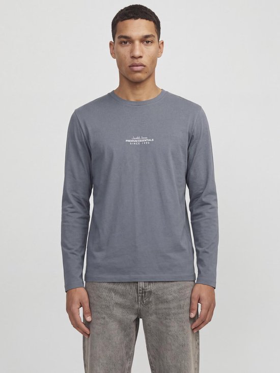 Een model van voren gezien, draagt een grijs shirt met lange mouwen met "Jack&Jones PREMIUM ESSENTIALS SINCE 1990" print.