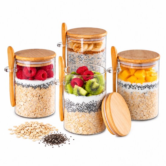 Vier glazen potjes met ontbijt van havermout, chiazaad, yoghurt en fruit. Potjes hebben bamboe deksels en lepels.