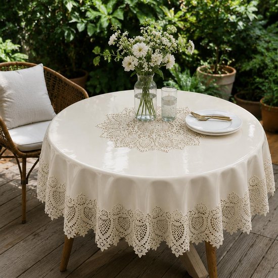 Ronde ivoorkleurige tafel in tuin met kanten rand tafelkleed, met bloemen en servies.