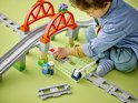 Jongetje speelt met LEGO Duplo treinbaan met oranje bruggen en grijze rails, groene en beige steunen.
