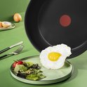Tefal koekenpan met een gebakken eitje wordt op een groen bord gegoten.