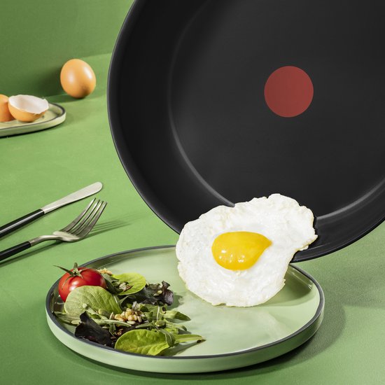 Tefal koekenpan met een gebakken eitje wordt op een groen bord gegoten.