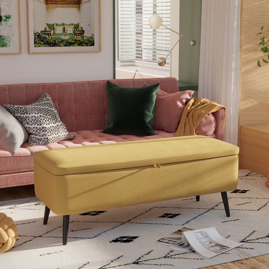 Gele opbergbank met textielbekleding in een woonkamer op een vloerkleed naast een roze bank.