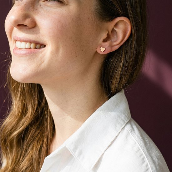 Glimlachend model met rosegouden hartvormige oorknopjes en een witte blouse.
