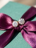 Goudkleurige 4 mm zirkonia oorknopjes op een groene doos met een paarse satijnen strik.