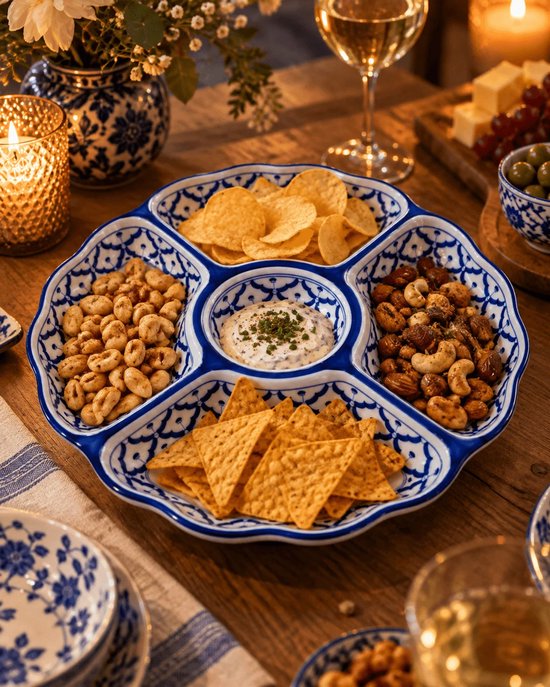 Blauw-witte tapasschaal gevuld met chips, nootjes en een romige dip op een sfeervol gedekte tafel.