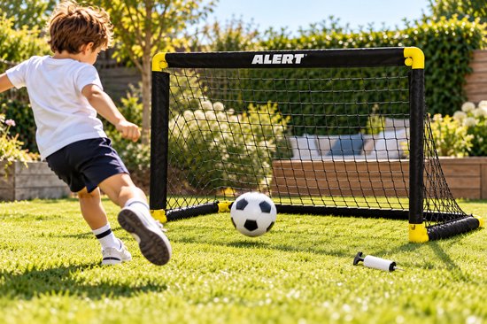 Jongen in wit shirt en blauwe short trapt een voetbal in een Alert voetbaldoel met geel frame en zwart net in de tuin.