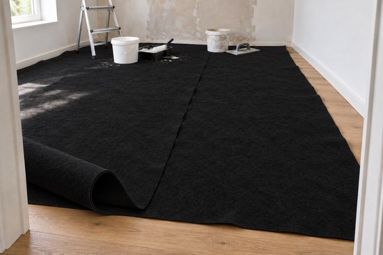 Zwart vilt wordt op een houten vloer uitgerold in een kamer in verbouwing met een ladder en verfbenodigdheden.
