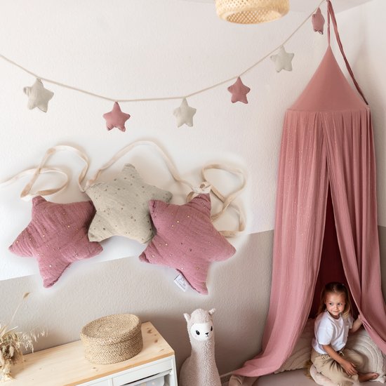 Roze en beige stoffen sterslinger met gouden accenten, opgehangen boven een speelhoek met een roze hemeltje en kind.