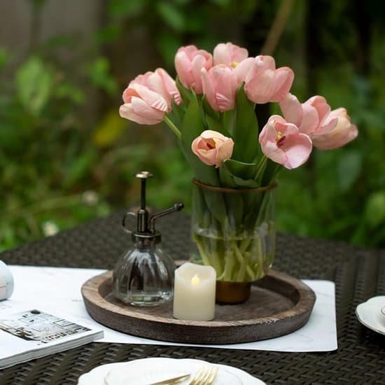 Rond houten dienblad met een vaas met roze tulpen, een glazen verstuiver en een led-kaars op een witte ondergrond.