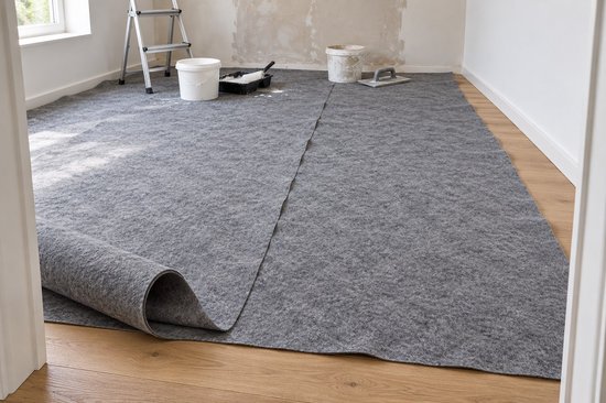 Grijze viltbekleding uitgerold op een houten vloer in een ruimte met schilderspullen.