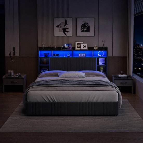 Donkergrijs gestoffeerd tweepersoonsbed met opbergruimte in het hoofdbord en blauwe LED verlichting. De kamer is verduisterd.