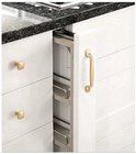 Een uitgetrokken keukenkast met een gouden handvat en een zichtbare, smalle, uittrekbare plank met metalen stangen.