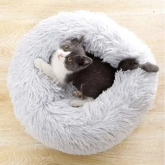 Grijze en witte kat ligt in een comfortabele, ronde, pluizige grijze mand.