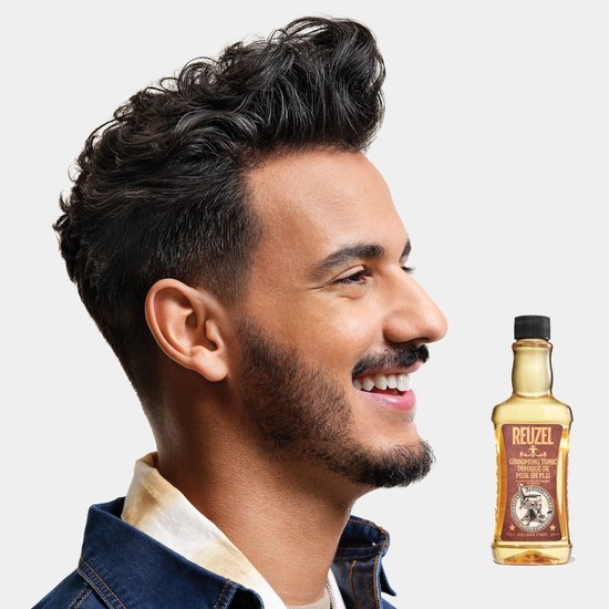 Lachende man met donker haar en baard, naast een fles Reuzel Grooming Tonic op een witte achtergrond.