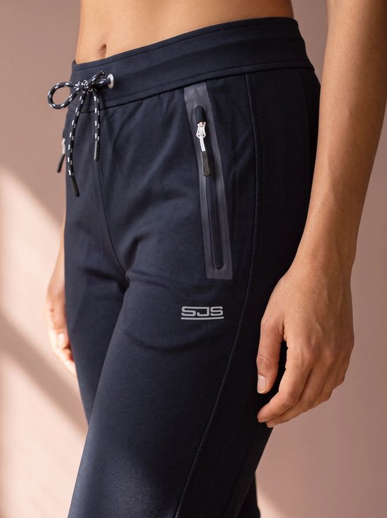 Close-up van zwarte sportbroek met SJS-logo, ritszak en gestreept trekkoord.