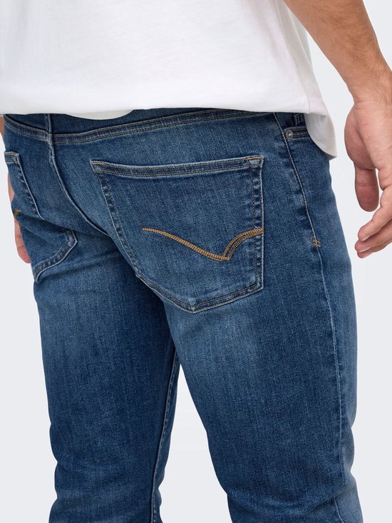Detail van de achterzak van een donkerblauwe slim-fit jeans met bruin stiksel.
