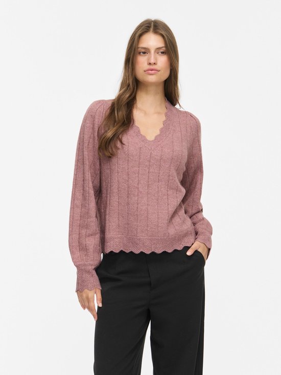 Model in roze VILA trui met V-hals, geribde details en geschulpte randen, gecombineerd met een zwarte broek.