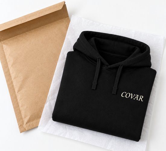 Zwarte hoodie met COVAR-logo in crèmekleurige letters, liggend op wit papier naast een bruine envelop.