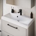 Witte wastafel op een beige zwevend meubel met matzwarte kraan, handgrepen en accessoires tegen een tegelwand.