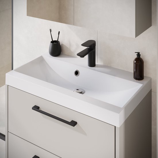 Witte wastafel op een beige zwevend meubel met matzwarte kraan, handgrepen en accessoires tegen een tegelwand.