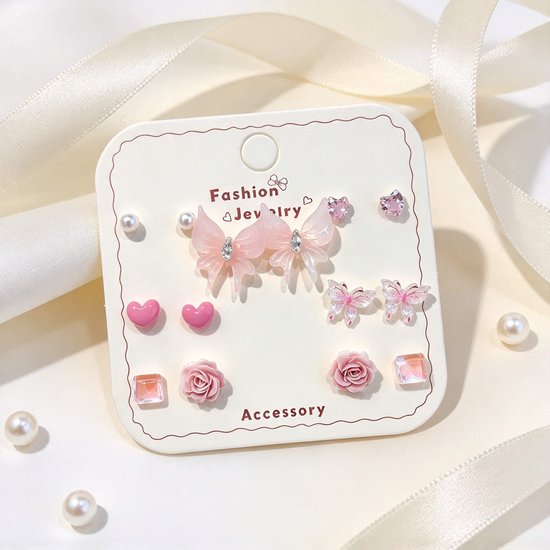 Set van 7 paar roze oorbellen met vlinders, harten, bloemen en kristallen op een Fashion Jewelry kaart.