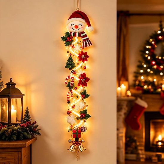 Verlichte sneeuwpop kersthanger met poinsettia's, cadeautje en gouden klokjes, hangend aan een muur.