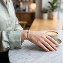 Vrouw draagt een zilveren armband met een enkele zirkonia aan een tafel met een kop koffie.