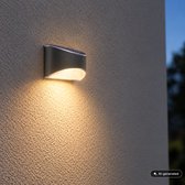 Antracietkleurige solar buitenwandlamp aan een gestucte muur met warm wit neerwaarts licht.