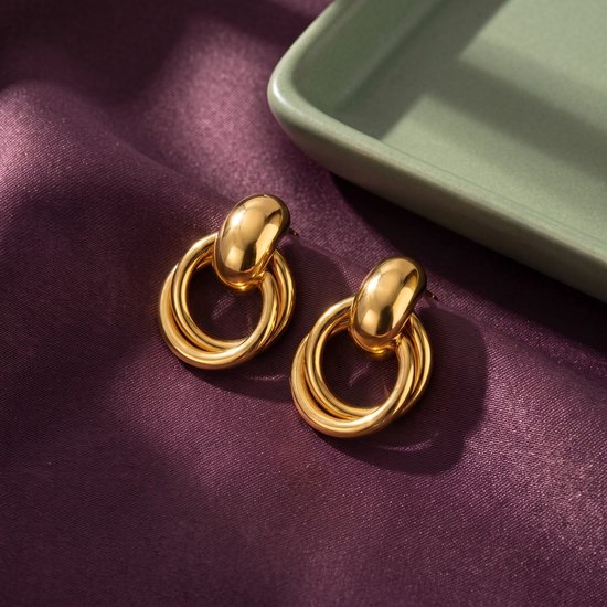 Goudkleurige Lundholm oorknopjes met dubbele ringen, elegant gepresenteerd op een paarse satijnen stof.