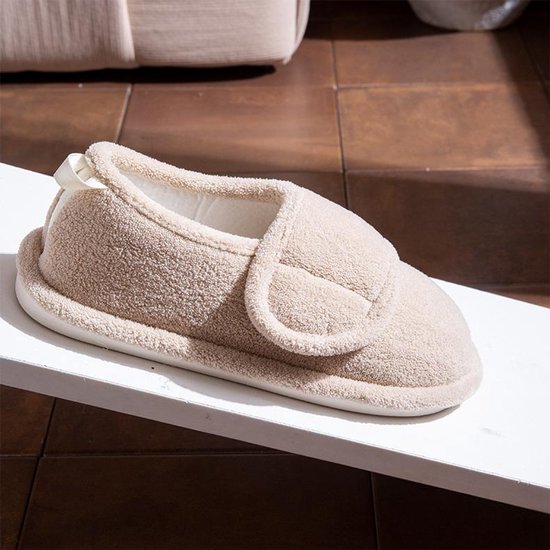 Beige pluche pantoffel met verstelbare klittenbandsluiting op een verhoogd wit oppervlak.